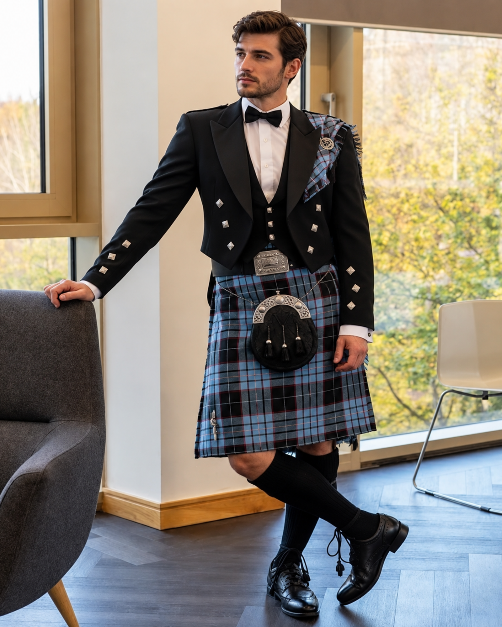 Man wearing a blue tartan men’s scottish kilt with black, red and white lines, styled with a black Prince Charlie jacket, waistcoat, bow tie, sporran and black hose